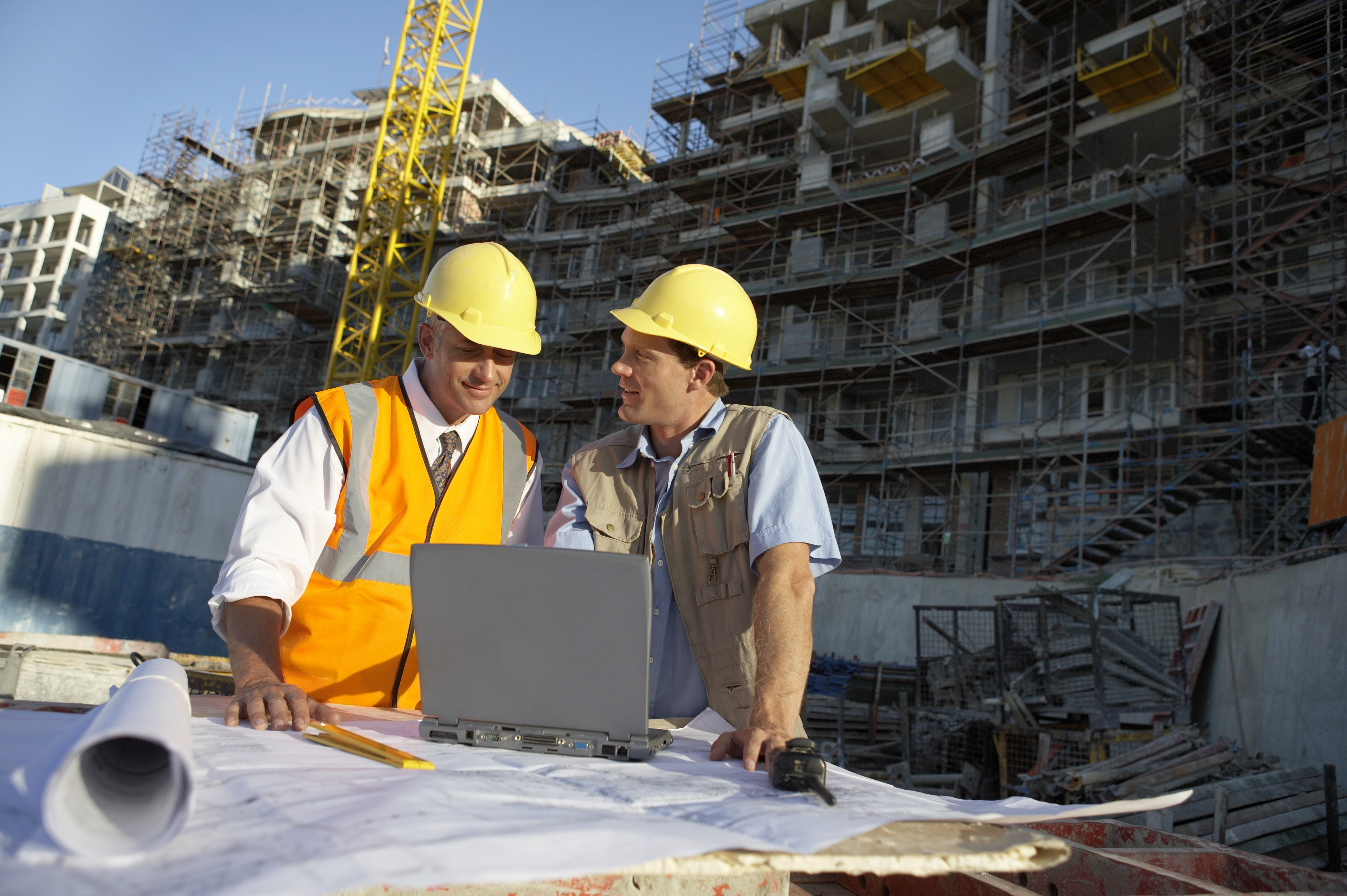 two workers wearing hard hats inspecting building site plan